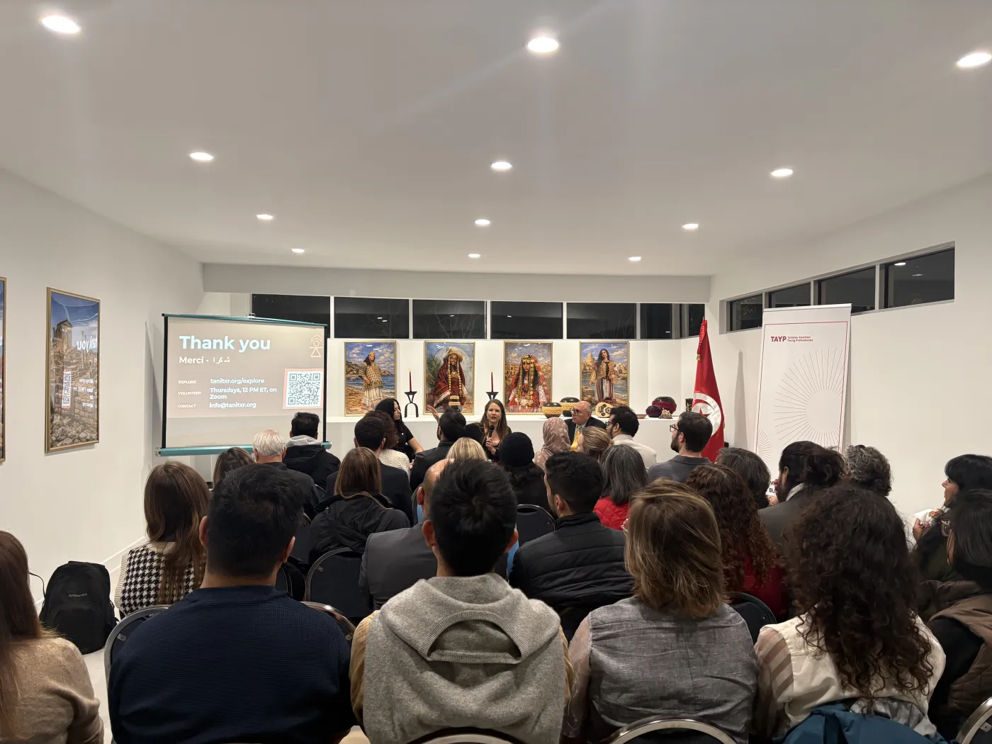 The room at the Ambassade de Tunisie during the talk, the audience facing the speakers et a screen that reads Merci